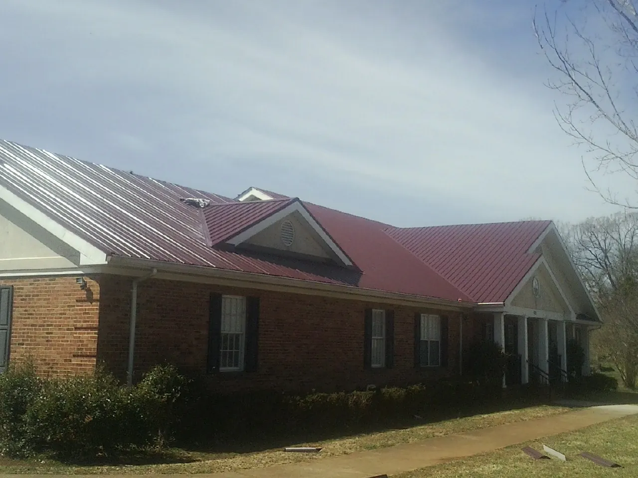 Red metal roof with gabled entries on a long brick building, from a Hail Damage Roof Repair job in Bolton
