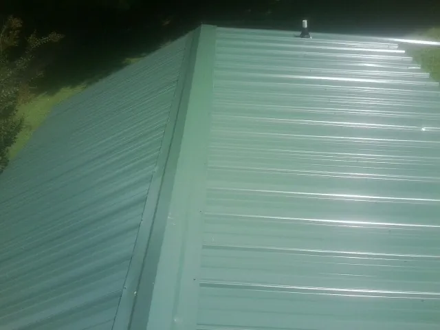 New green metal panels meeting at the ridge of a roof — Flat Roof Repair work by our crew in Bolton