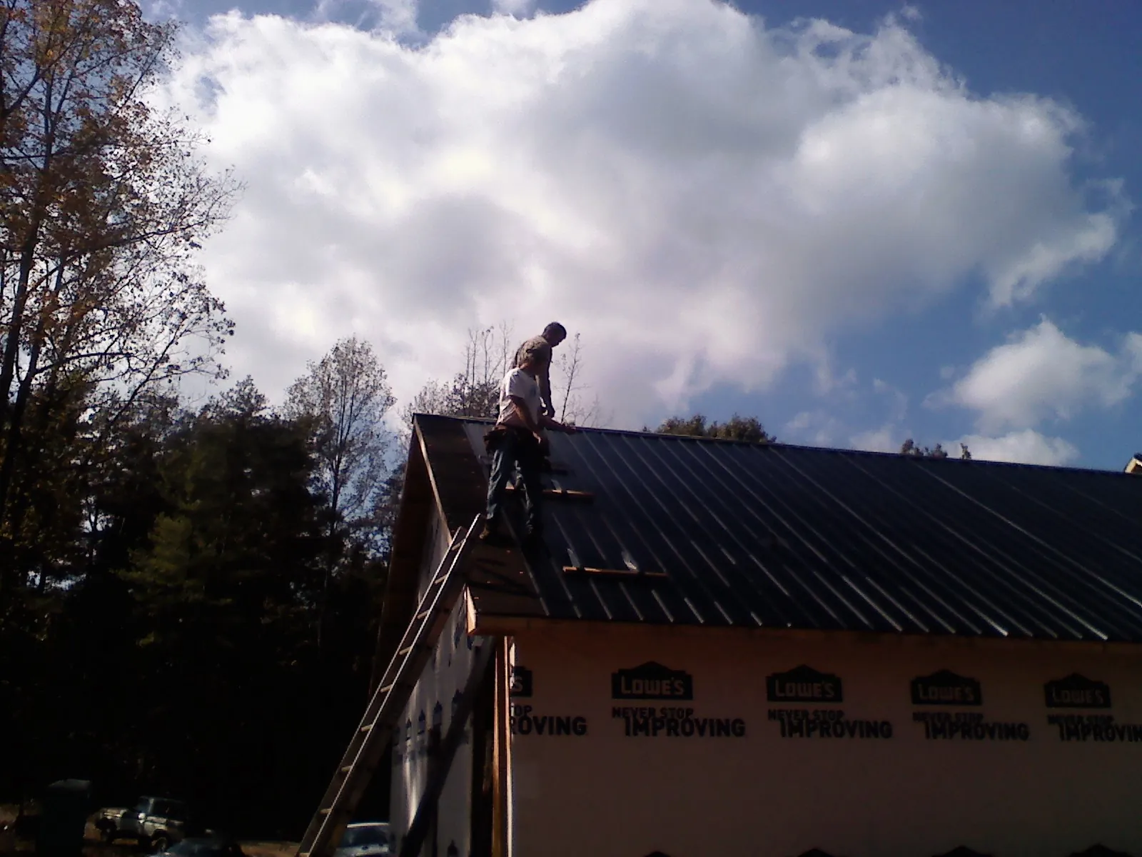 Roofer fastening dark metal panels high against a cloudy sky, from a Roof Inspection job in Bolton
