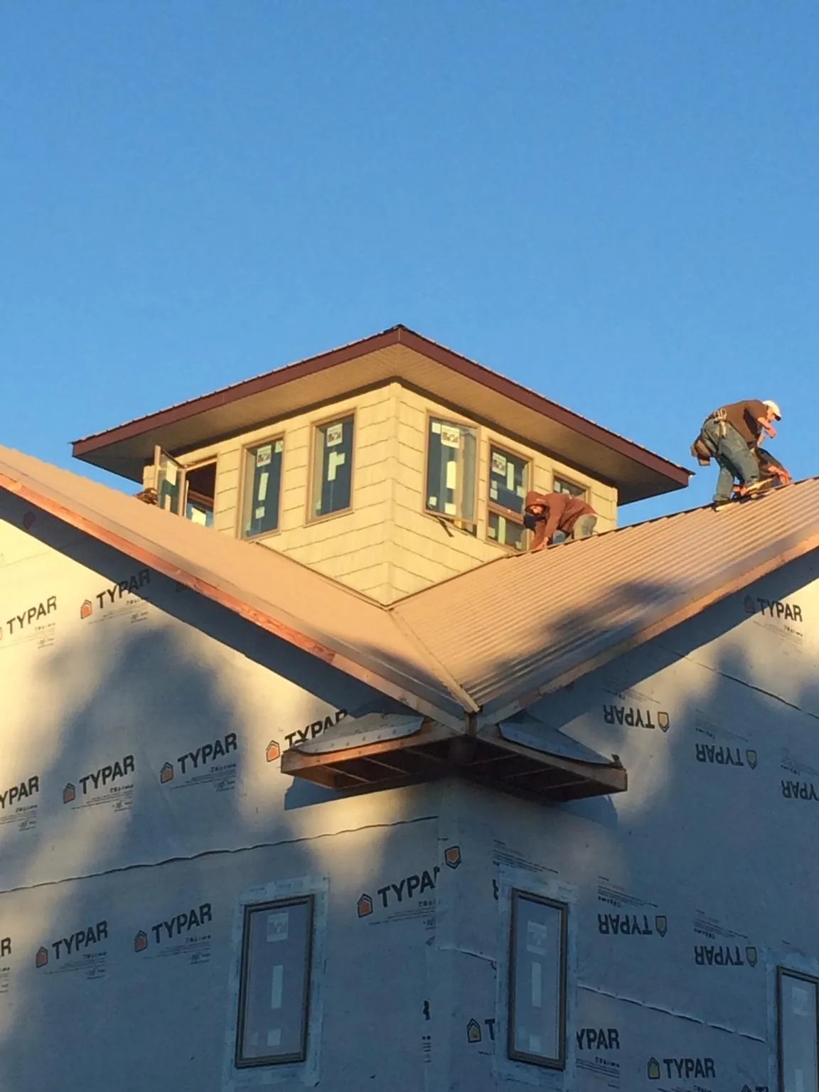 Roofers working around a rooftop cupola on a new metal roof at sunset — Roof Waterproofing in Bolton by Roofing Brothers